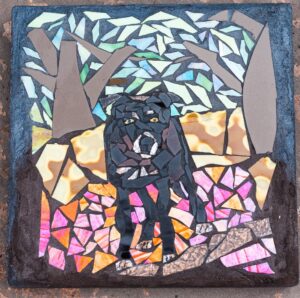 Early mosaic of a black dog in a forest scene, created with colorful, uneven stained glass and ceramic pieces in a wabi-sabi style.